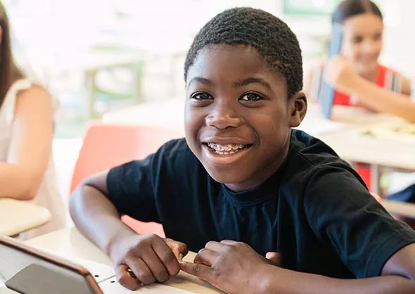 Boy sitting at desk smiling with metal braces.